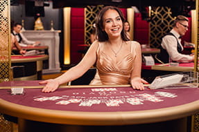 En kvindelig dealer sidder ved et rødt kortspilsbord og smiler til kameraet.