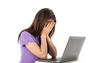 Kvinde sidder med hovedet i hænderne foran en laptop