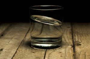Et glas vand på et træbord med en sort baggrund.