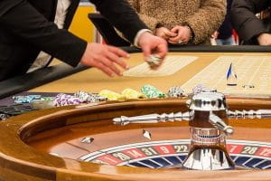 I forgrunden ses et roulettehjul. Bagved ses roulettebordet og hænderne på en dealer, som flytter rundt på casinochips.