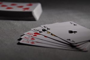 Fem spillekort med billedsiden opad og en anden bunke spillekort i baggrunden. 