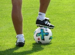 Nærbillede af en bold og en mands ben og fødder. Den ene fod er placeret på fodbolden.