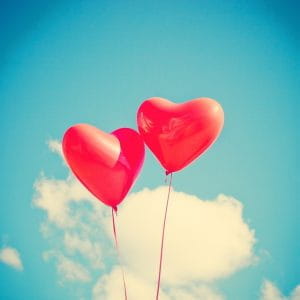 To hjerteformede balloner svæver på himlen.