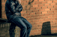 En man sidder på et mustenshegn og taler i telefon.